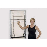 Femme posant à côté Pilates Wall Unit 5-en-1 montée au mur mettant en échelle humaine et accès aux barres métalliques
