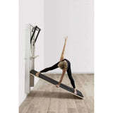 Posture yoga triangle sur Pilates Wall Unit 5-en-1 utilisant plateau incliné noir comme support d'équilibre et étirement
