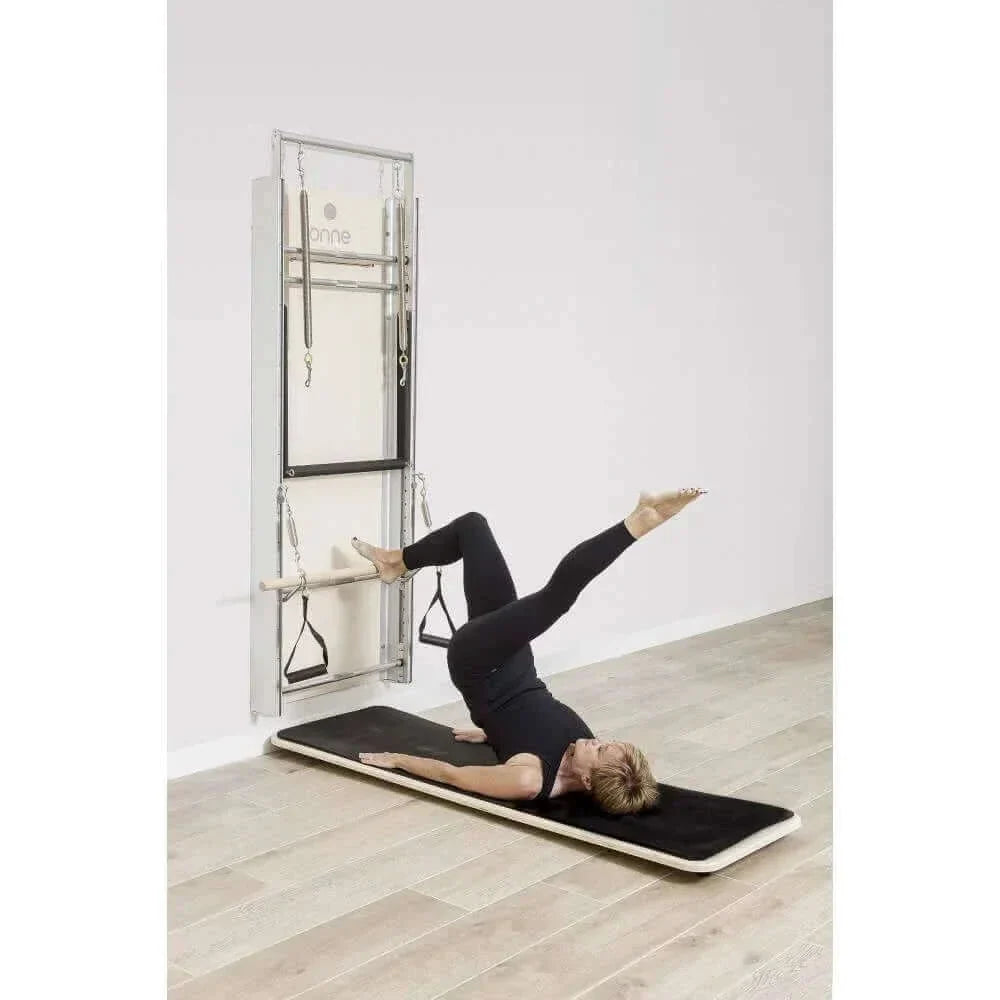Exercice abdominal sur Pilates Wall Unit 5-en-1 avec femme allongée sur plateau incliné noir utilisant sangles de traction