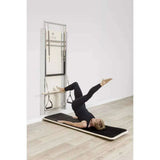 Exercice abdominal sur Pilates Wall Unit 5-en-1 avec femme allongée sur plateau incliné noir utilisant sangles de traction