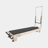 Reformer Pilates Elite en bois clair avec structure chromée et coussins noirs, vue de trois-quarts