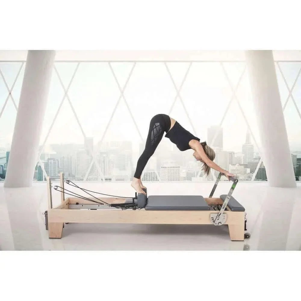 Femme utilisant Reformer Pilates Elite en bois clair pour posture chien tête vers le bas